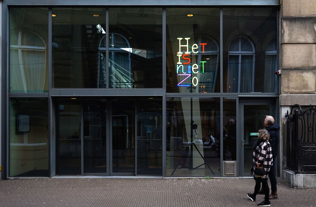 In gekleurde neonletters op een vier meter hoog statief staat Het is niet zo. Het kunstwerk staat bij ingang van het Logement van de Heeren van Amsterdam. Het is het gebouw waar de Parlementaire Enqu�te Commissie van de Tweede Kamer zitting heeft. Het kunstwerk is gefotografeerd na de restauratie op 13 december 2022