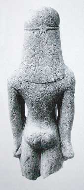 Kouros, achterzijdezijde, een kleine stenen naakte jongen. Het is een votiefgeschenk uit de ori&euml;ntaliserende periode +/- 600 voor Chr., van de Grieken. Omdat het beeldje in Amsterdam te bezichtigen is heeft het de naam &lsquo;de Amsterdamse Kouros&rsquo; gekregen.