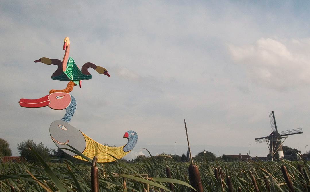 een windobject draaiend op drie punt. Het staat in het riet in de polder. het is een grote eend met op zijn kuif vier zwamen halsen met kop, &copy; Andr&eacute; Boone